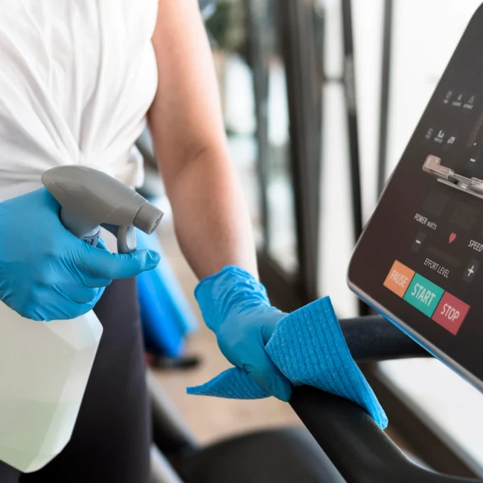 woman-with-gloves-cleaning-gym-equipment-with-solution